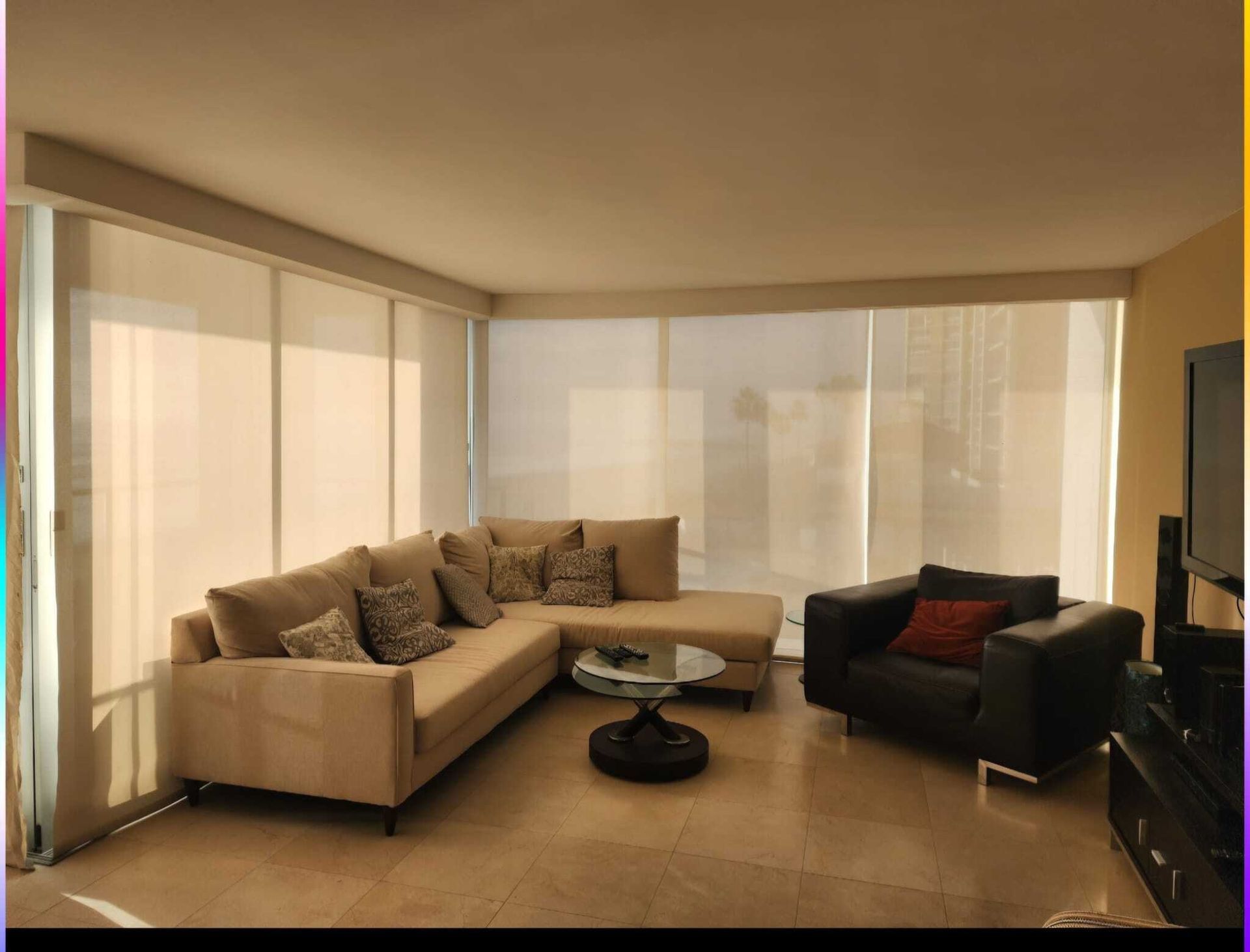 Living room with beige sectional sofa, black armchair, and sheer window shades.