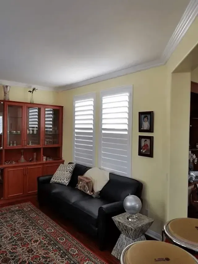 Living room with black leather sofa, white shutters, and a wooden cabinet.