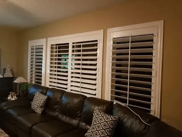 Living room with white shuttered windows above a dark leather couch.