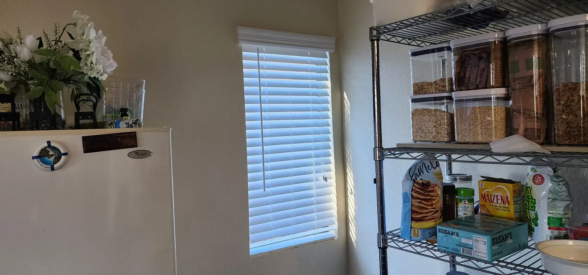 A kitchen scene with a window and a shelf holding food containers and other supplies.