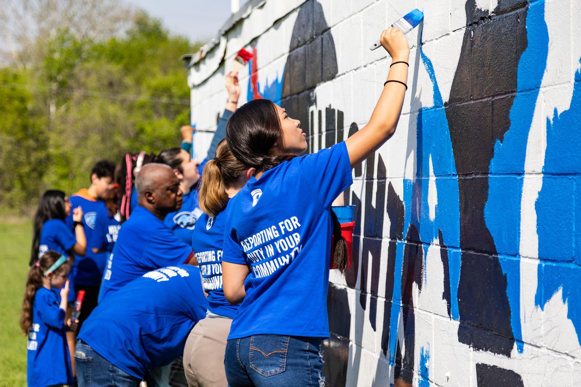 A group of people in blue shirts are painting a wall.