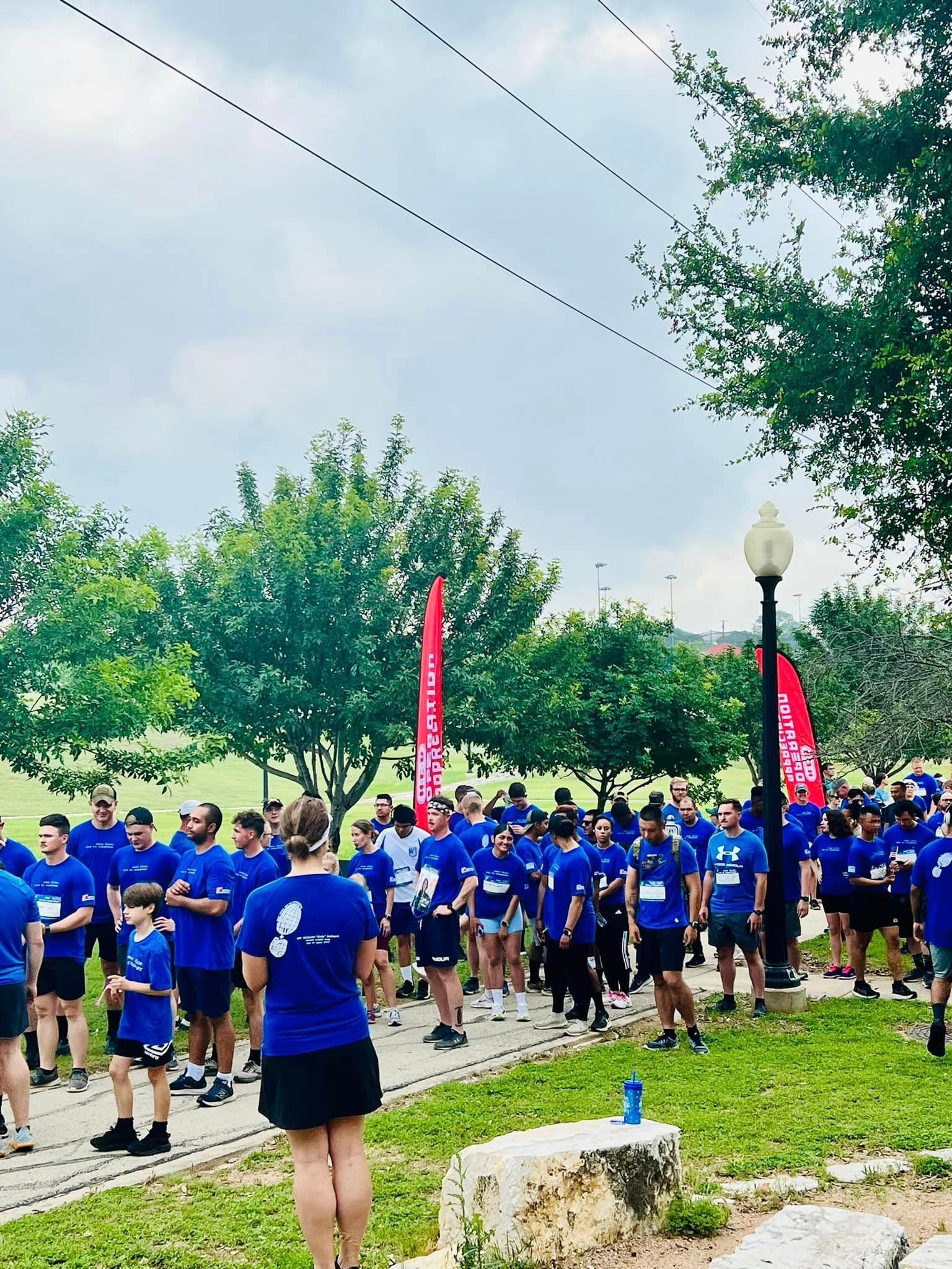 A large group of people in blue shirts are standing in a park.