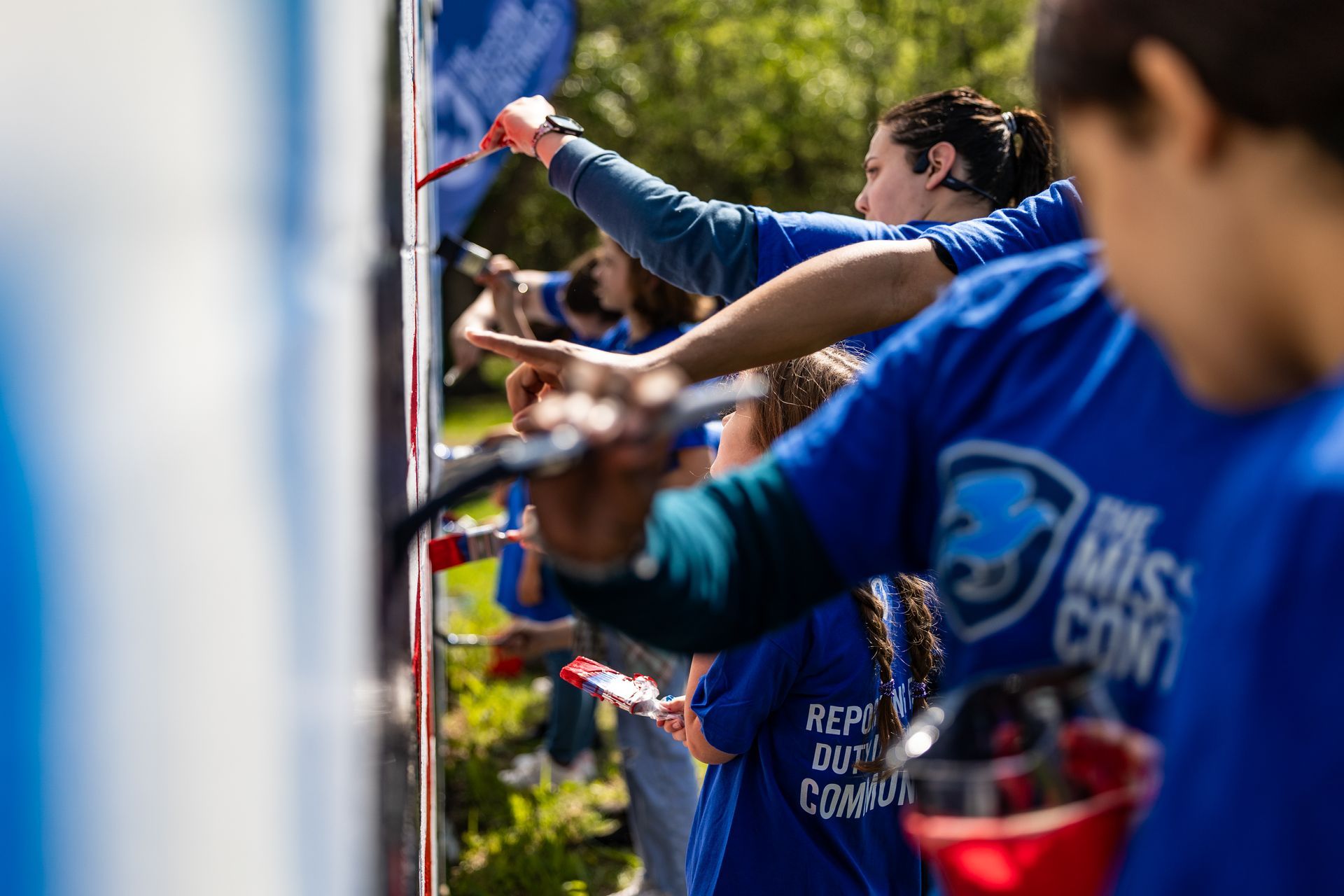 A group of people in blue shirts are painting a wall.