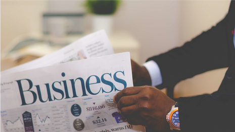 A man in a suit is holding a newspaper with the word business on it.