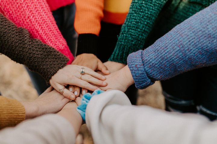 Diverse hands stacked together in a circle, wearing colorful sweaters, symbolizing teamwork.