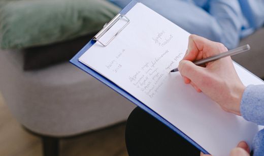 Hand writing notes on a clipboard with a pen in a casual indoor setting