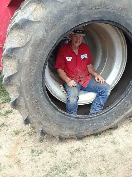 Man sitting inside a large tractor tire on a farm, wearing red shirt and blue jeans.