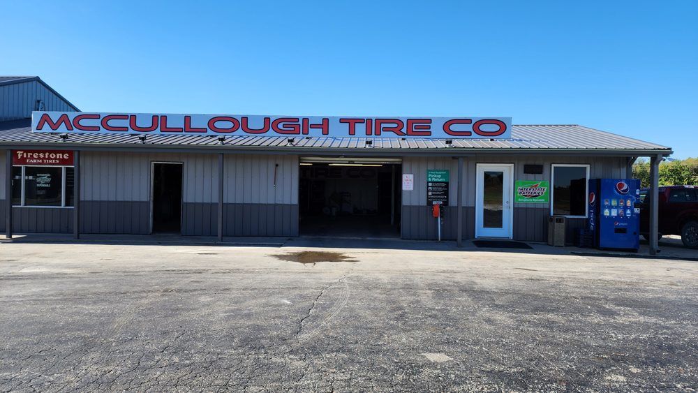 McCullough Tire Co. storefront with red sign, gray building, open bay, vending machine, and clear blue sky.