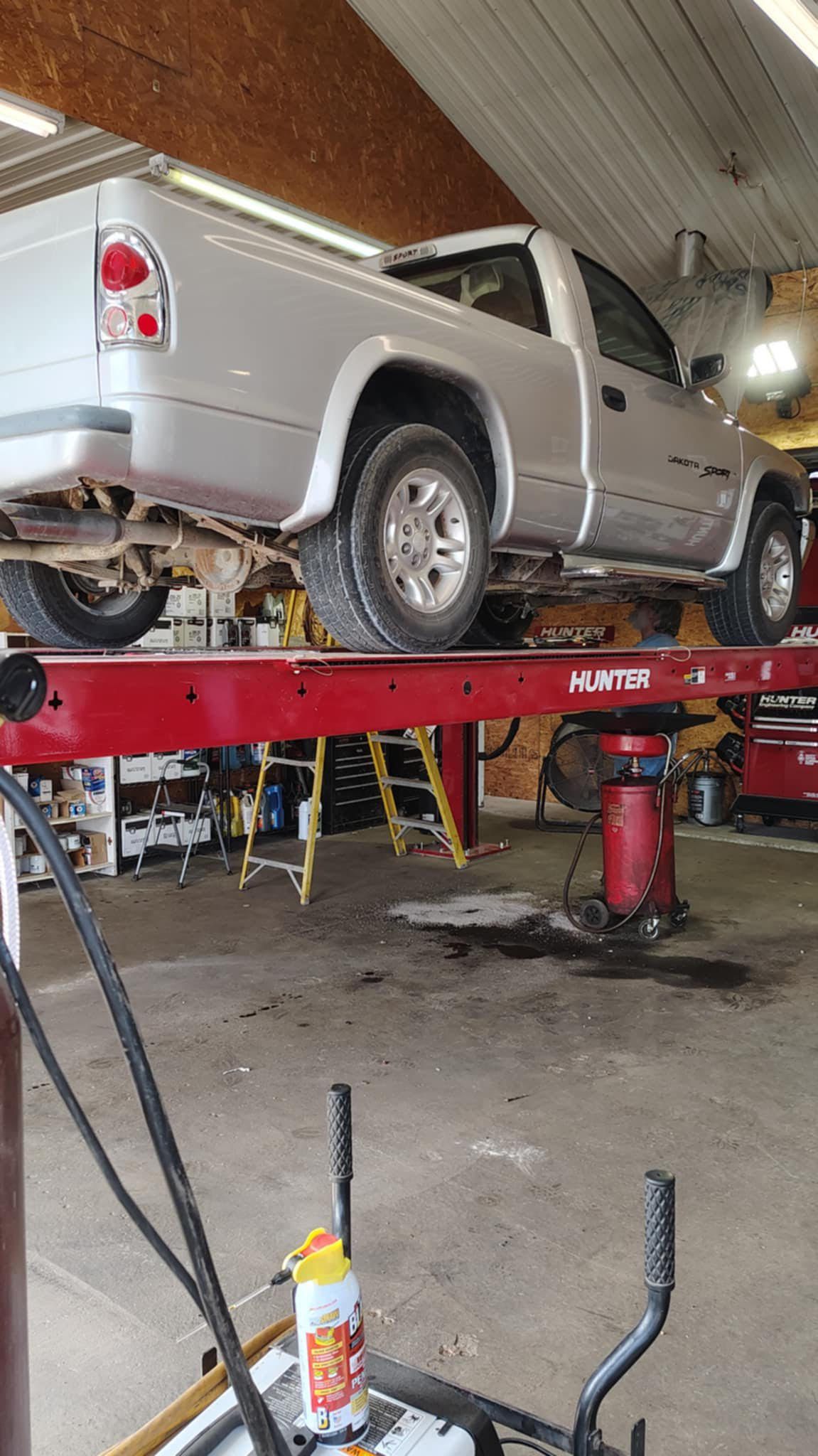Silver pickup truck on a red hydraulic lift inside a garage.