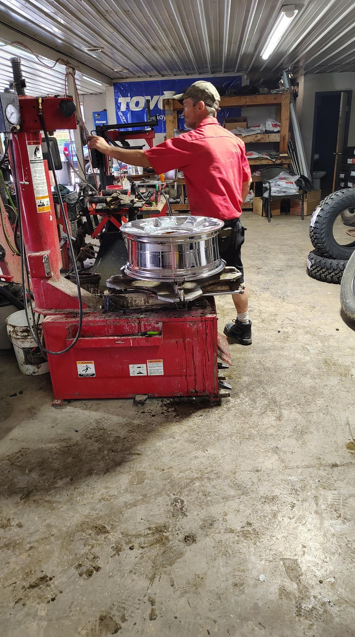 Mechanic in a red shirt working on a shiny wheel with a tire machine in a garage.