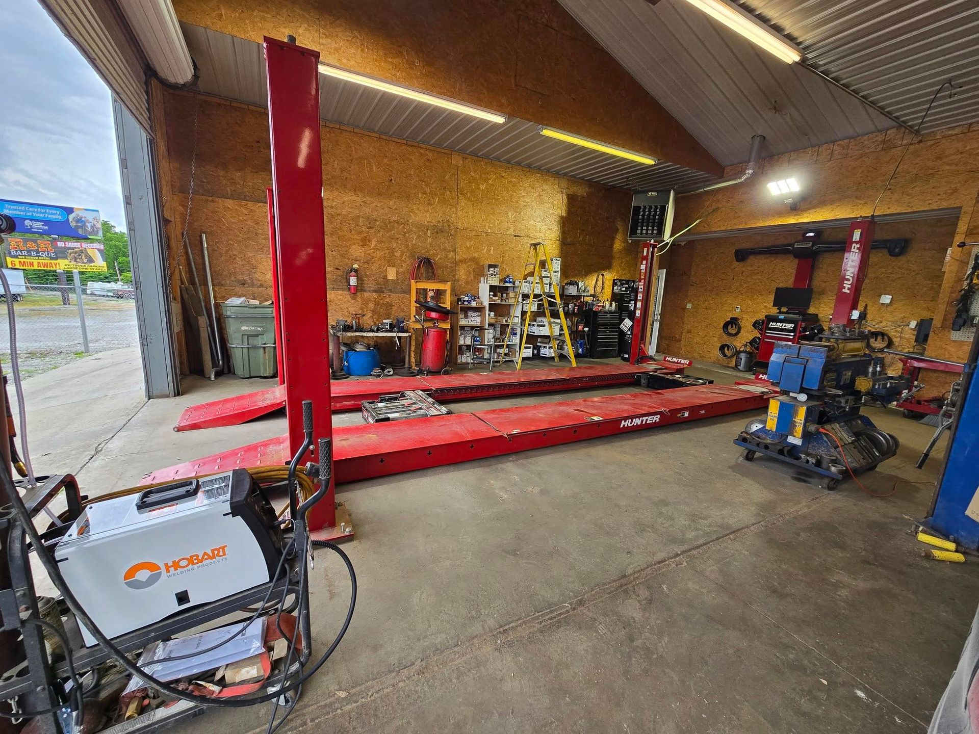 Red four-post car lift in a workshop; welding machine in foreground.