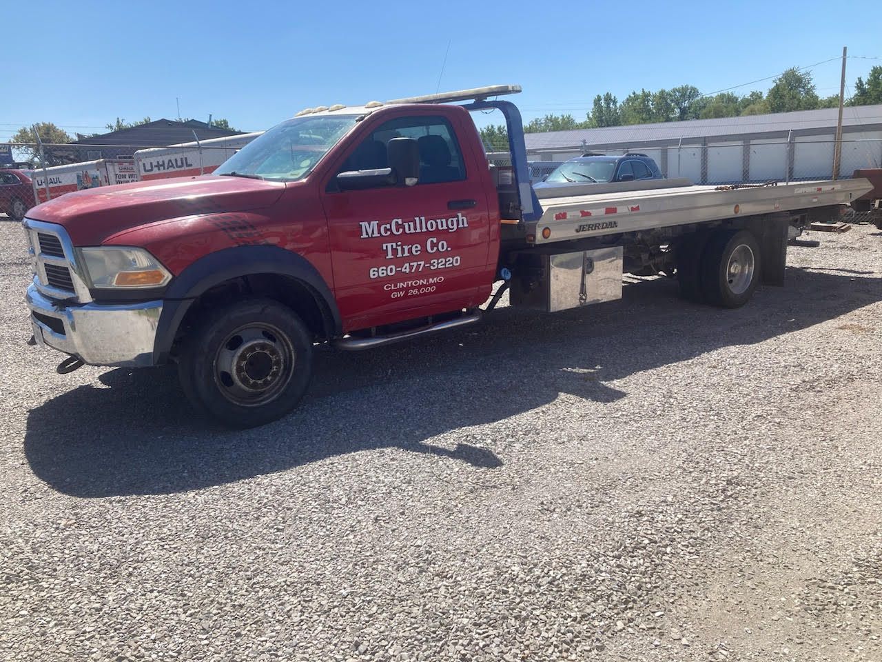 Red tow truck with a flatbed, parked on gravel. 