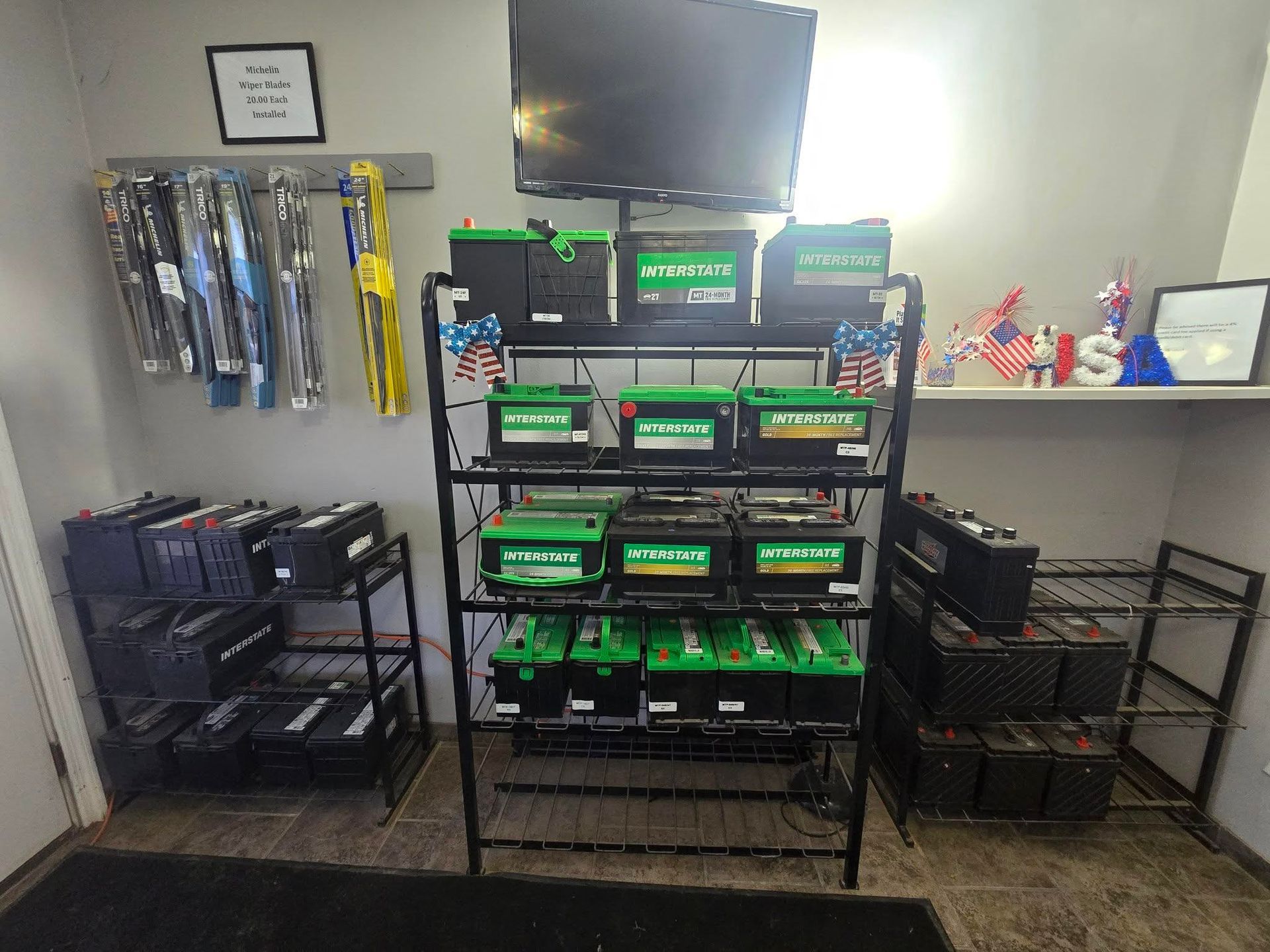 Car batteries displayed on metal shelves inside an auto shop. A TV is mounted above.