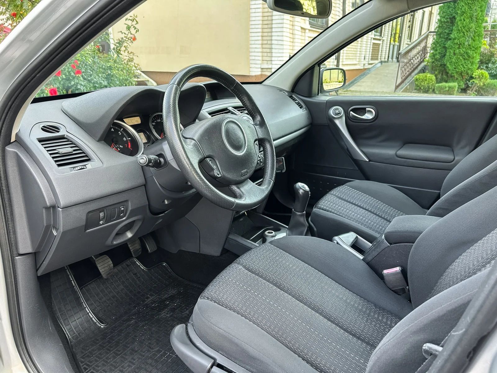 Car interior with black cloth seats, steering wheel, dashboard, and open driver’s door in daylight