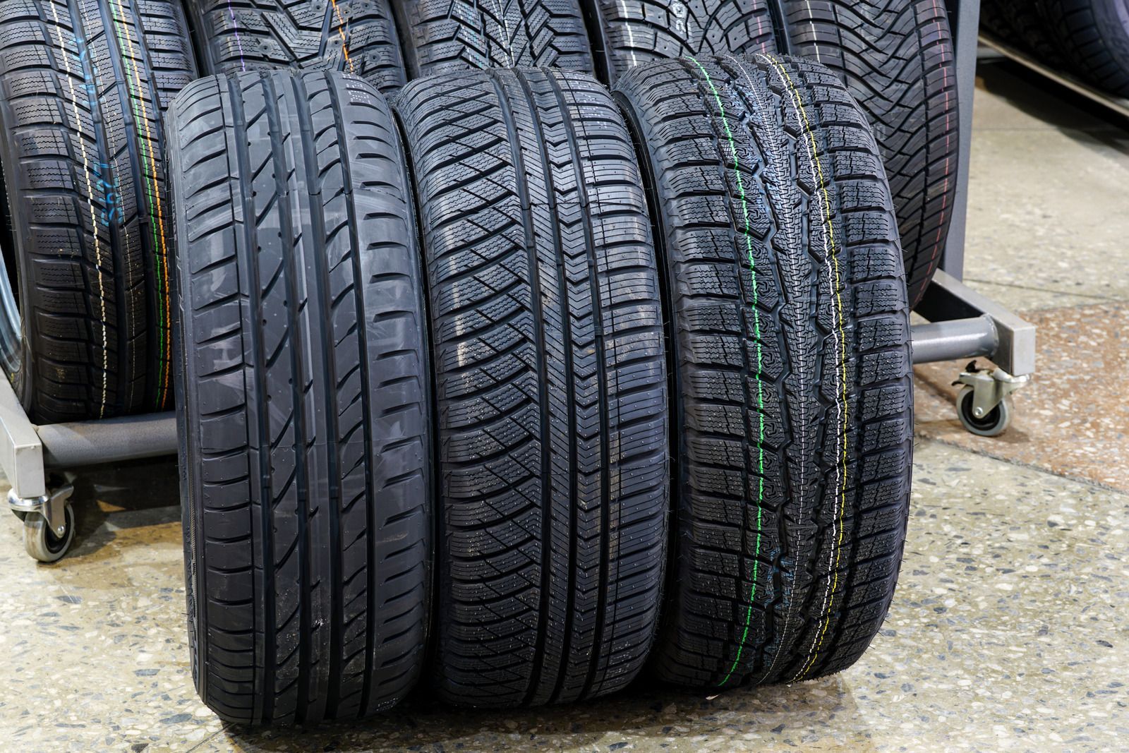 Stack of new black car tires on a concrete floor, with a wheeled cart in the background
