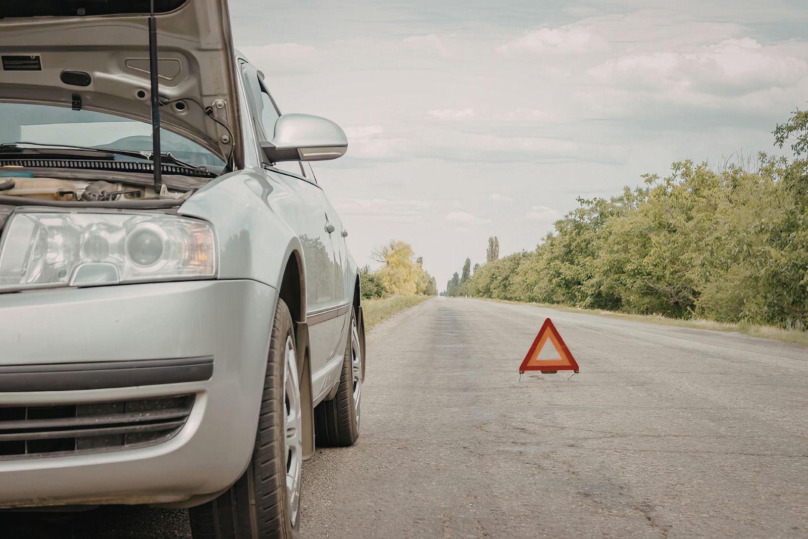 Silver car stopped on roadside with warning triangle on the pavement ahead