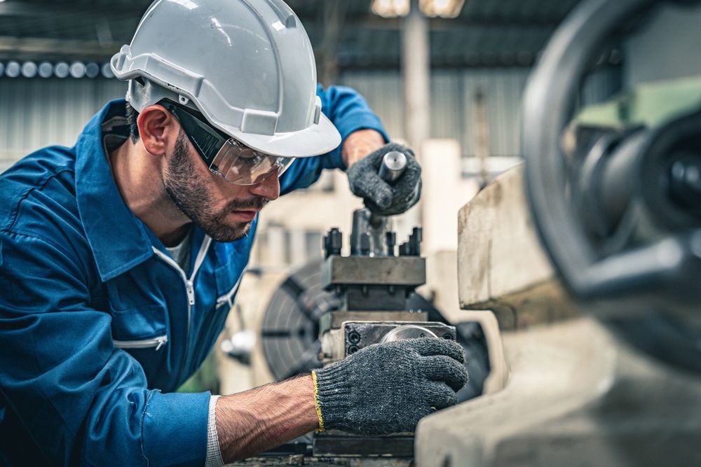 Mechanic in blue coveralls, safety glasses, and hard hat operating industrial machinery.