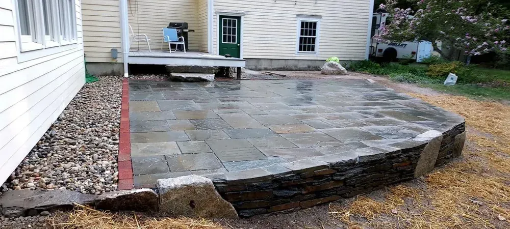 Stone patio beside a house, with a low step and a red border edging the edge