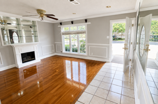 Bright empty living room with hardwood floors, tile entry, fireplace, and large windows showing a patio.