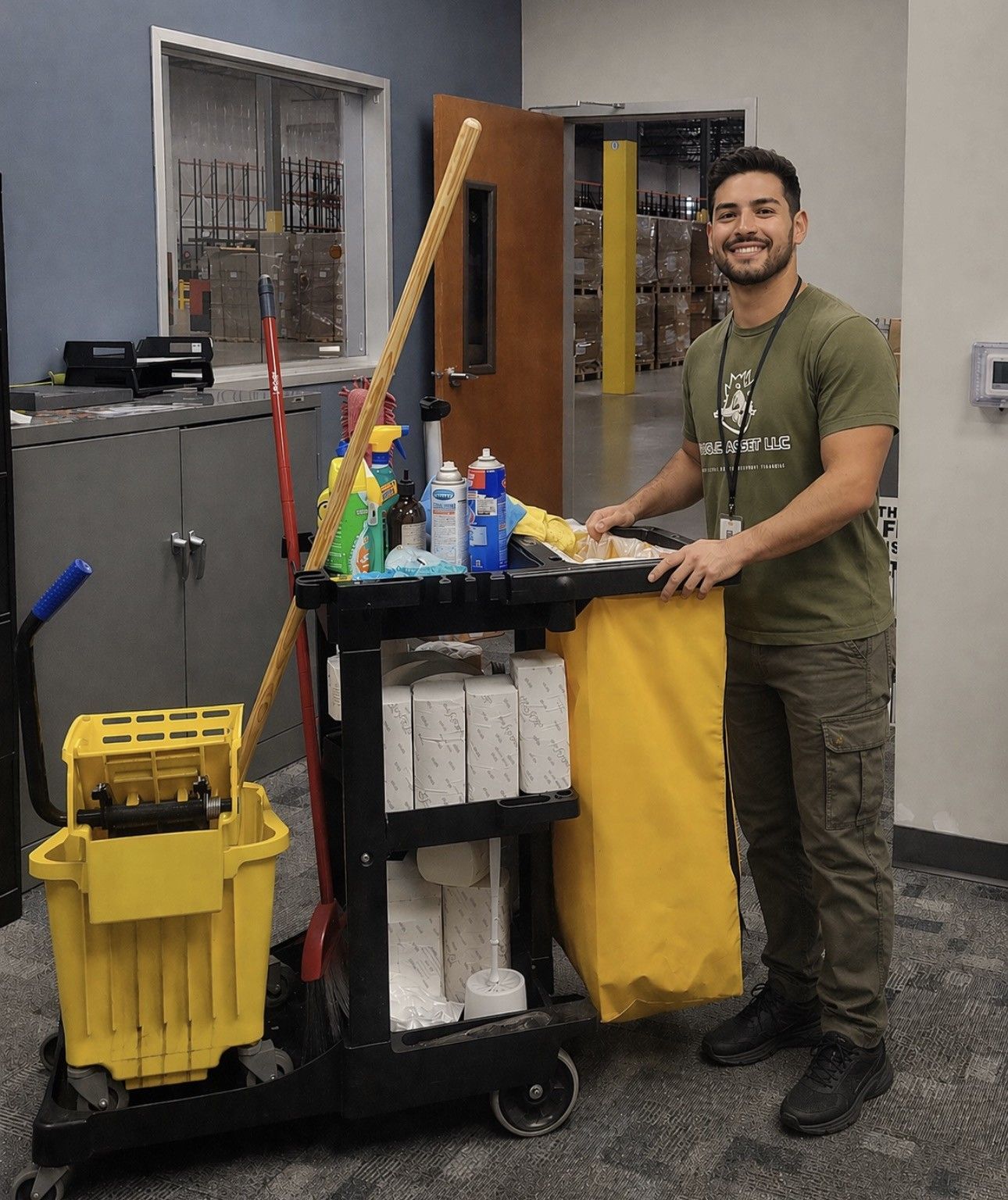 Man smiling beside a yellow janitorial cart in a hallway, holding a mop and cleaning supplies
