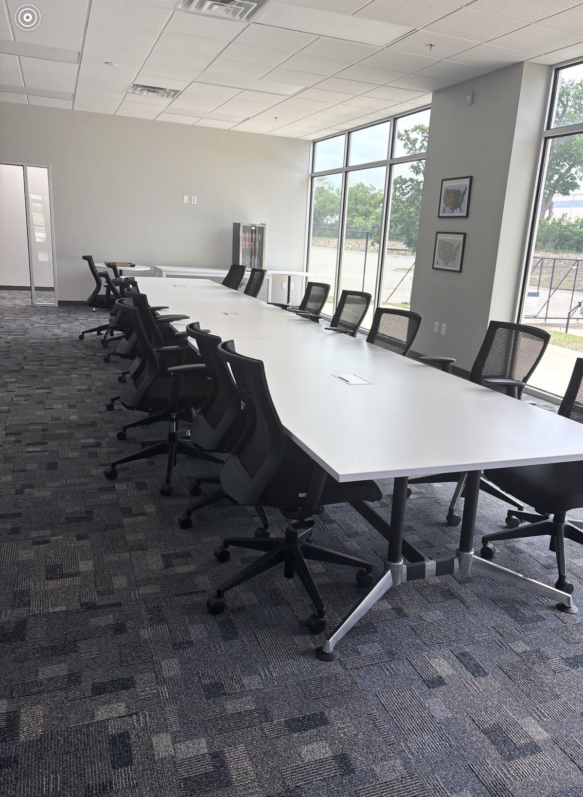 Empty conference room with long white table, black chairs, carpeted floor, and windows along the wall.