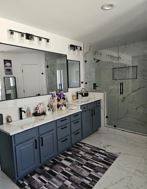 Modern bathroom with blue double vanity, large mirror, marble shower, and striped rug