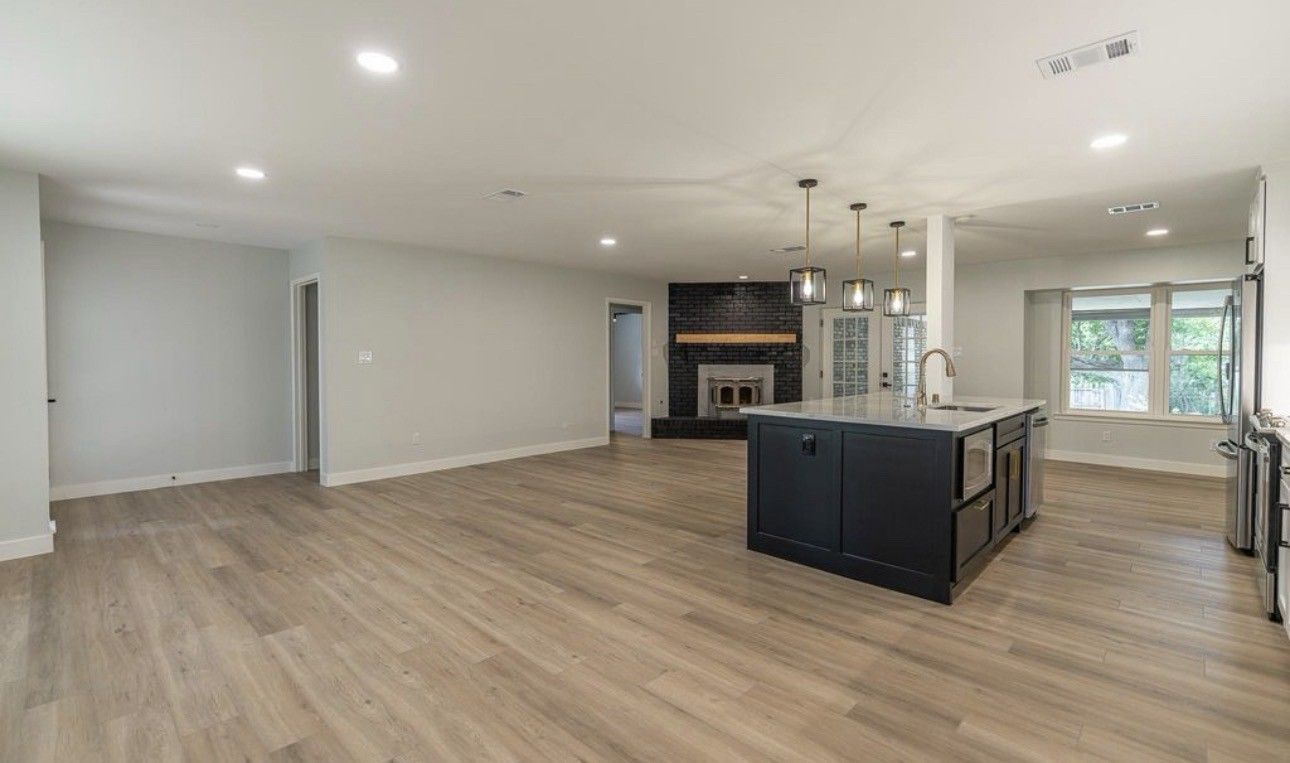 Spacious modern living room with wood floors, black kitchen island, and fireplace in the distance