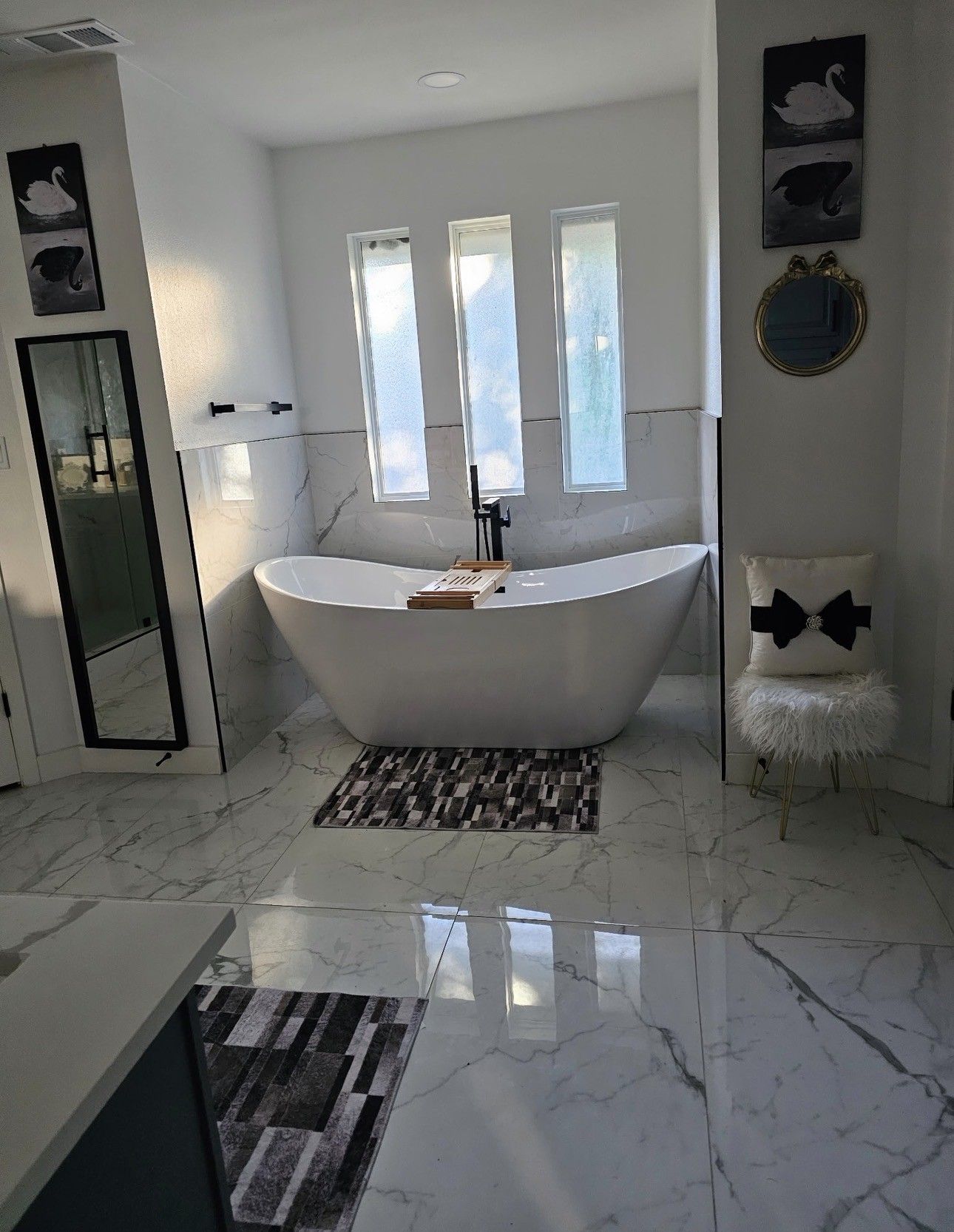 Modern bathroom with a freestanding tub, marble floor, tall mirror, and bright windows.