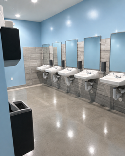 Bright, empty public restroom with four sinks, mirrors, blue walls, and tiled lower walls.
