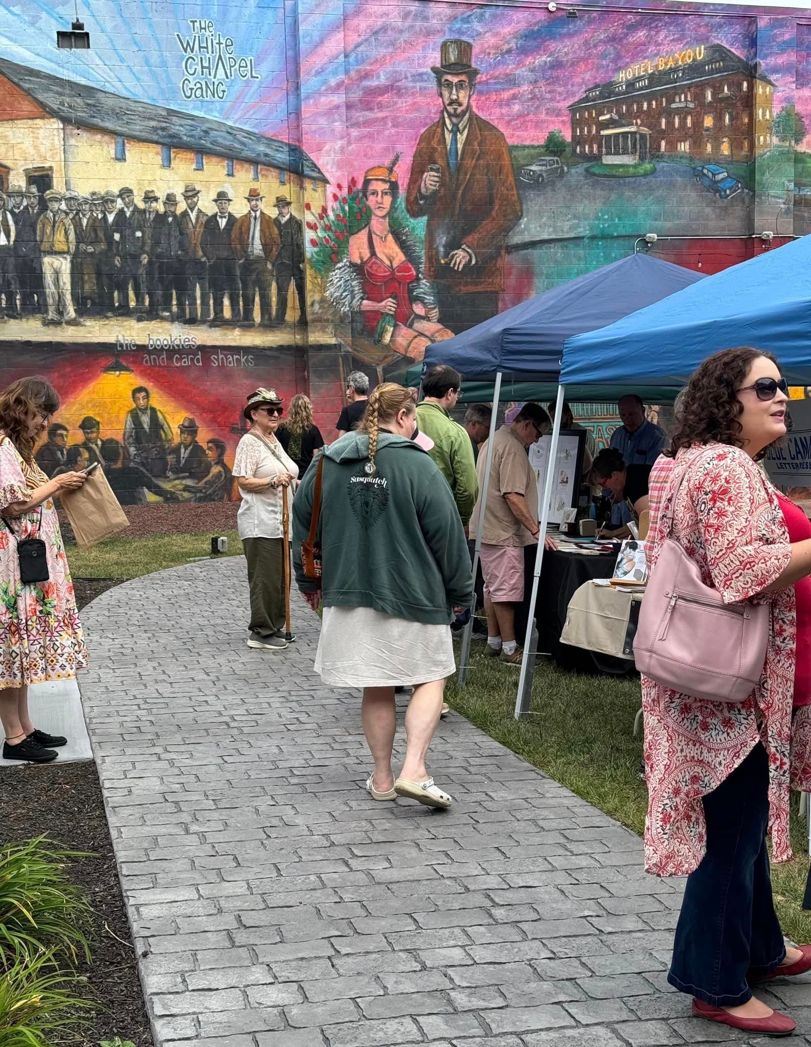 A group of people are standing on a sidewalk in front of a mural.
