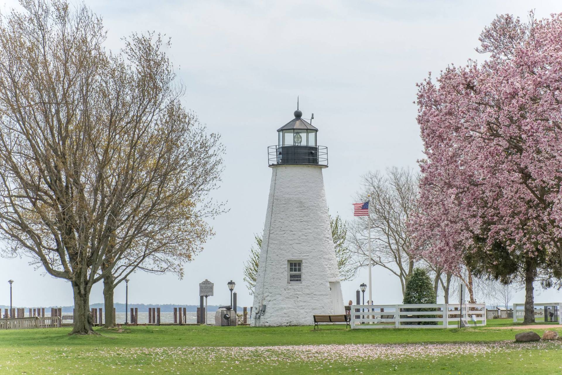 A lighthouse is surrounded by trees and flowers in a park
