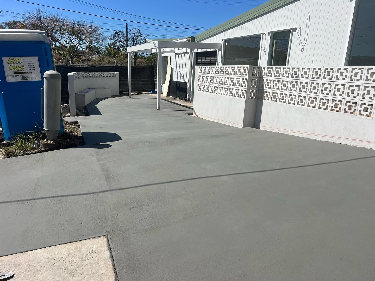 Concrete walkway beside a white building and wall, with a blue utility box and clear blue sky.