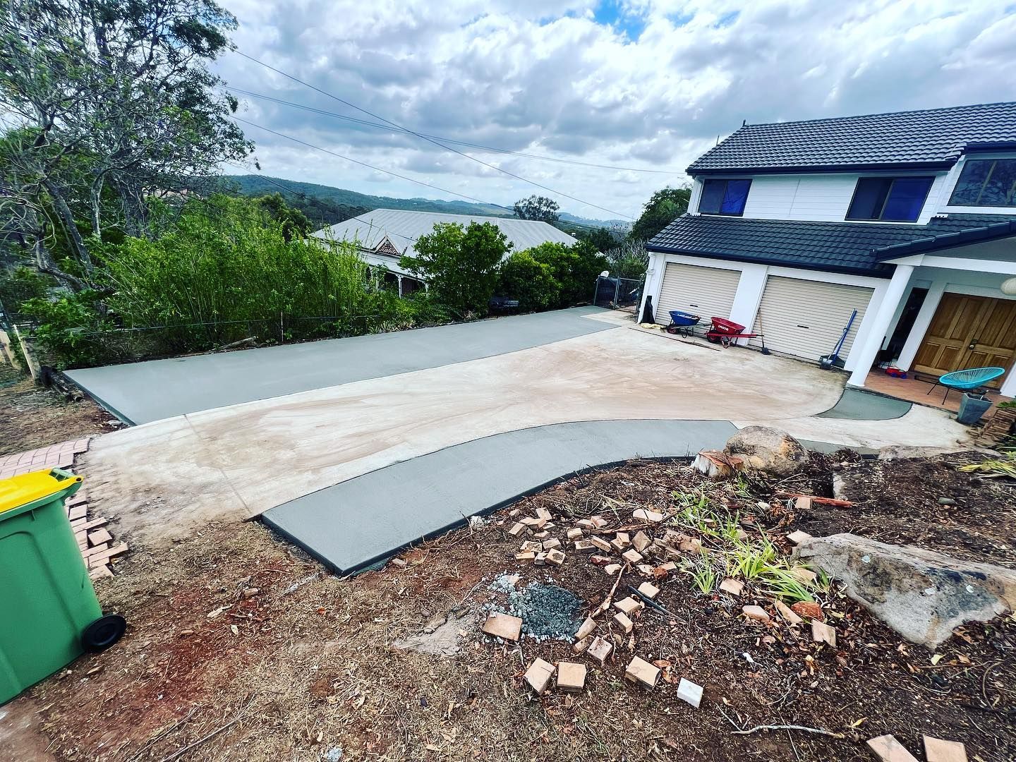 Damaged driveway slope beside a house, with broken concrete and debris on a hillside lot.