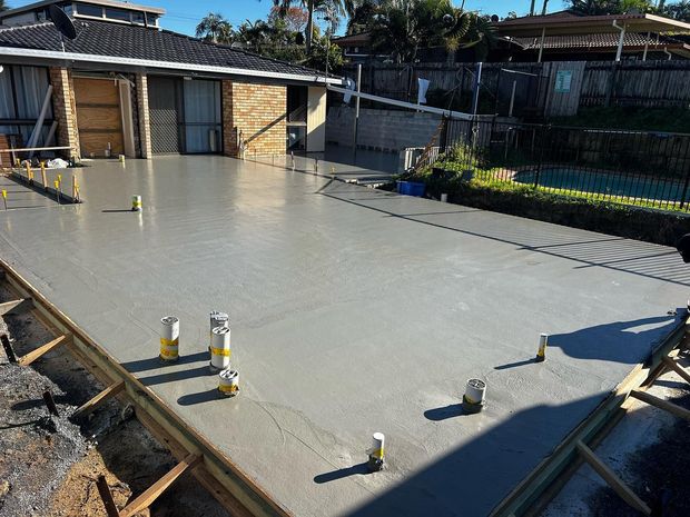 Fresh concrete slab being poured in a backyard construction site with house walls and pipes visible Fresh concrete slab being poured in a backyard construction site with house walls and pipes visible