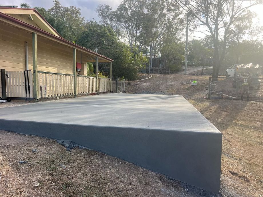 Concrete ramp beside a wooden building on a sloped dirt lot, leading up to a level platform Concrete ramp beside a wooden building on a sloped dirt lot, leading up to a level platform