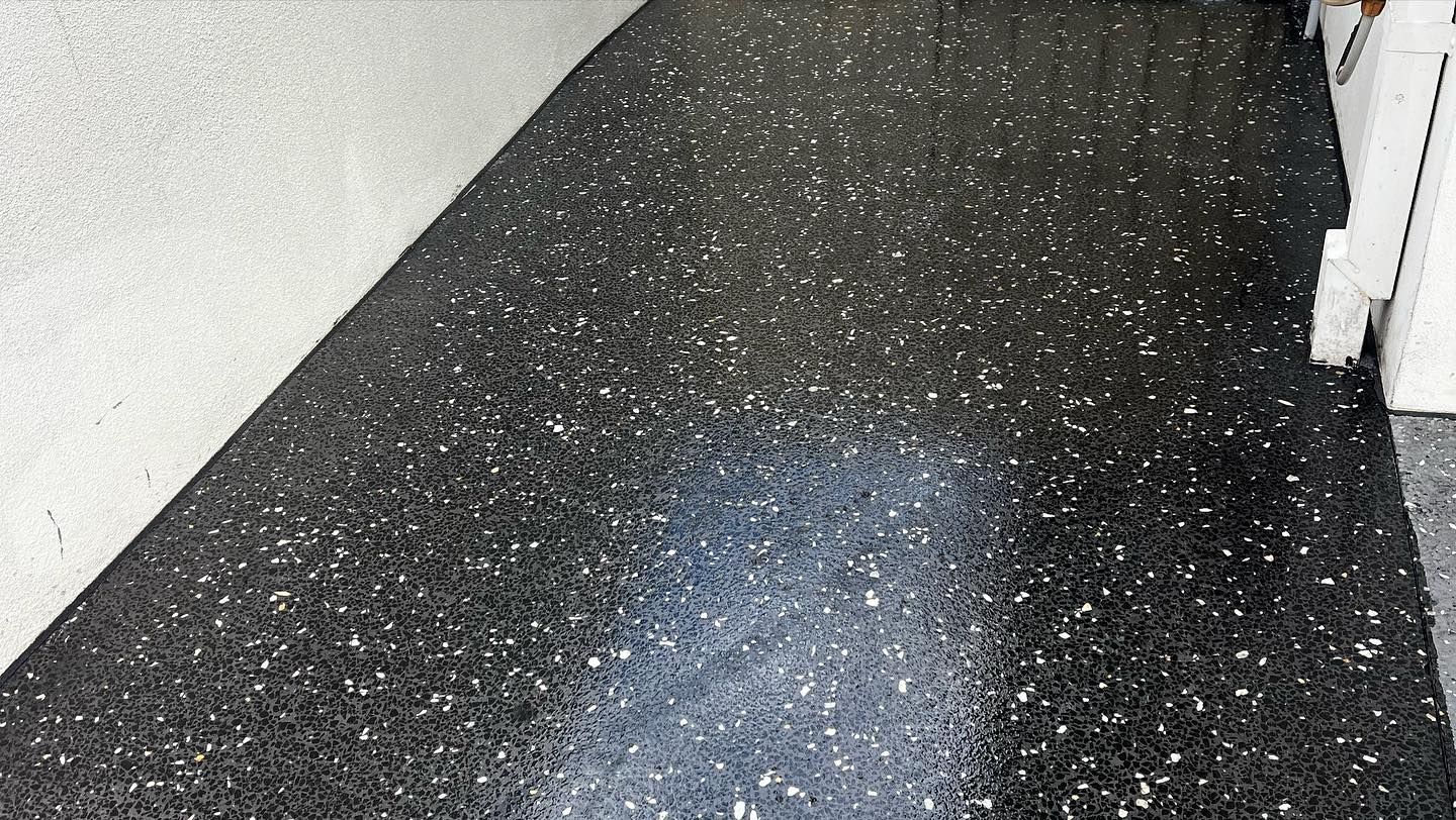 Black speckled floor in a narrow hallway with a bright light reflection on the surface