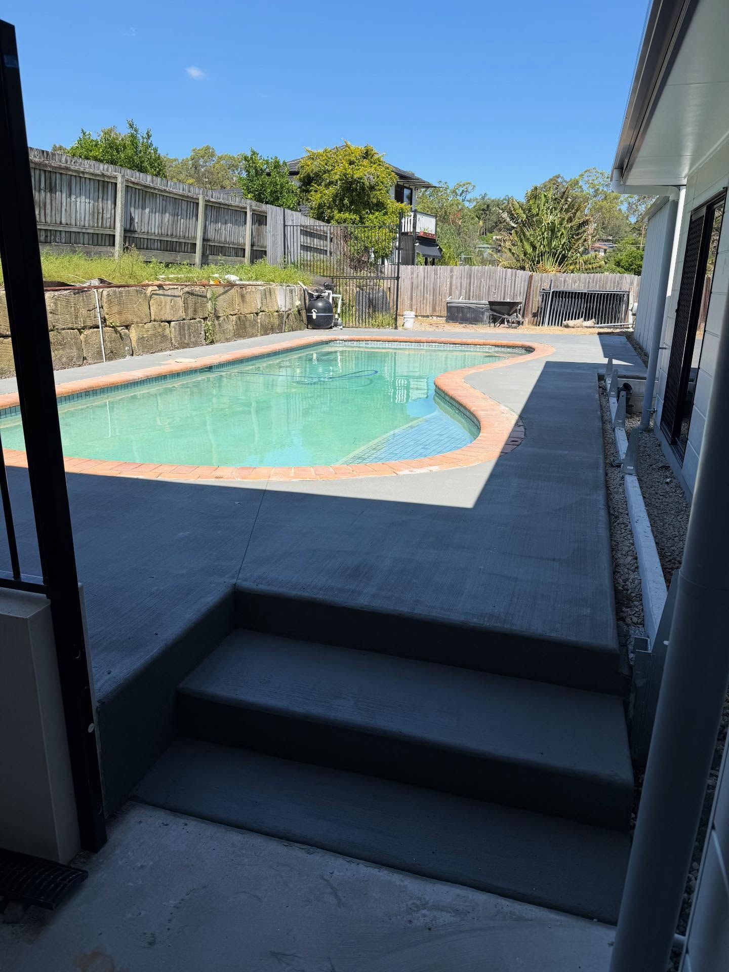 Backyard swimming pool with gray deck, stone wall, and stairs in the foreground