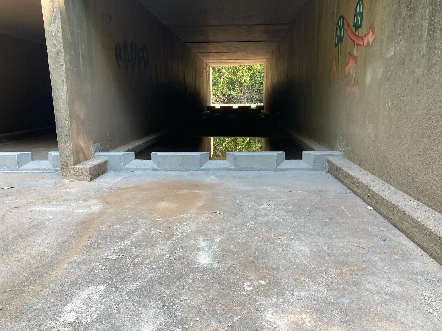 Concrete tunnel with shallow water reflecting a bright opening at the far end