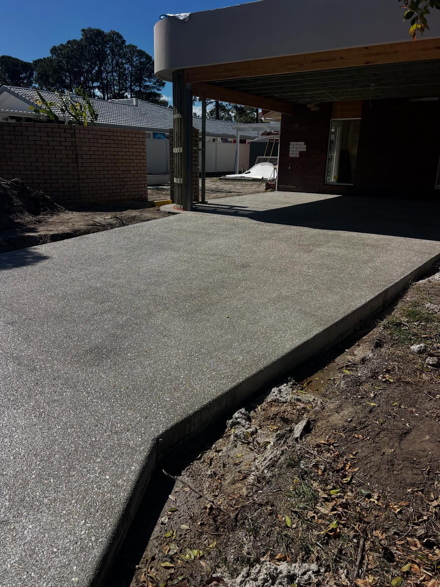 Concrete driveway leading to a shaded carport beside a brick wall and garden bed