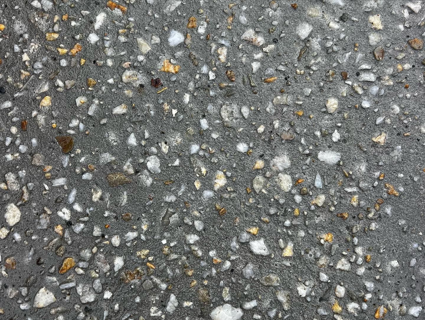 Close-up of gray asphalt pavement with small white, tan, and yellow stones.