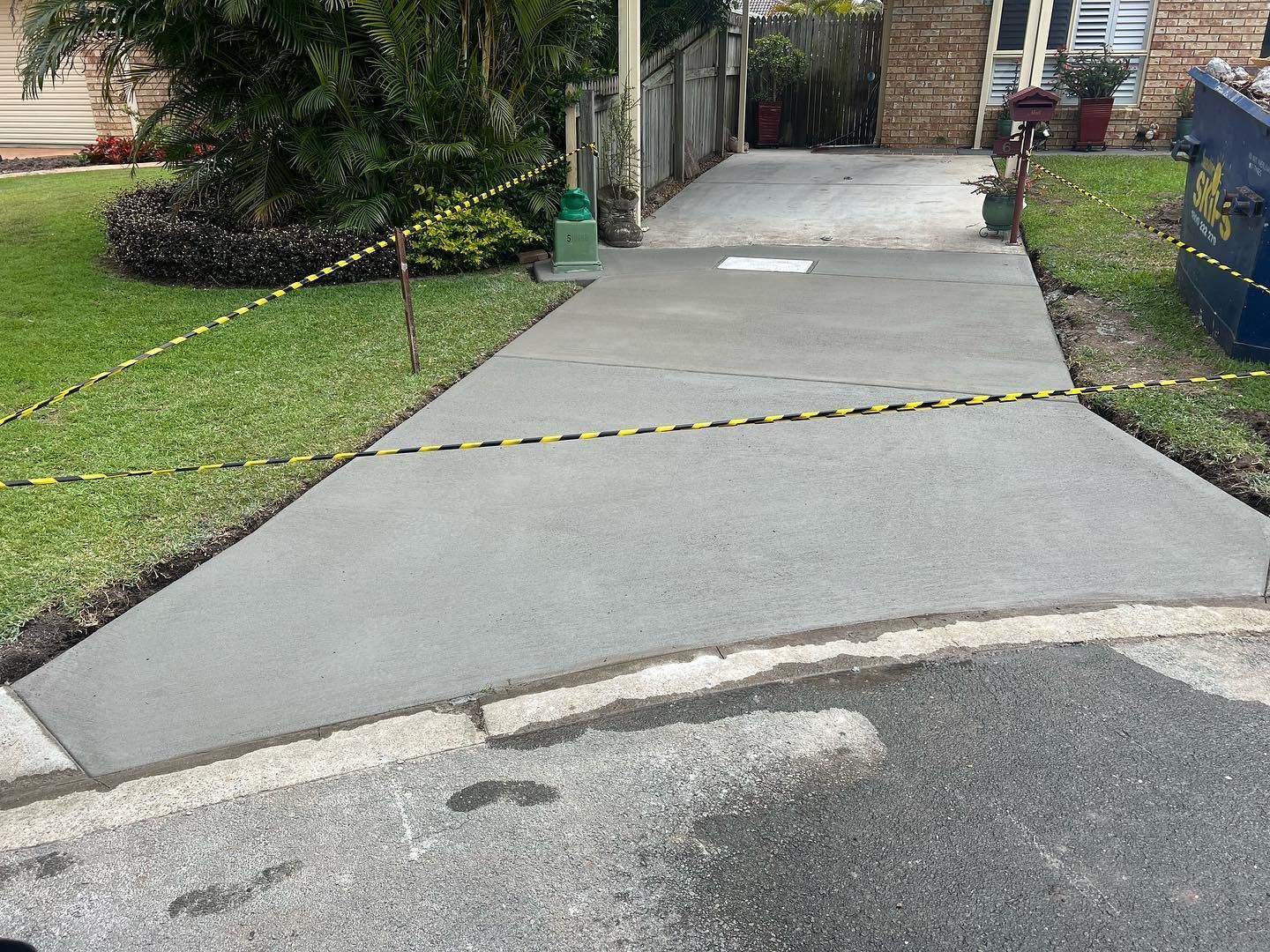 Cracked concrete driveway with yellow caution tape blocking the entrance near a house.