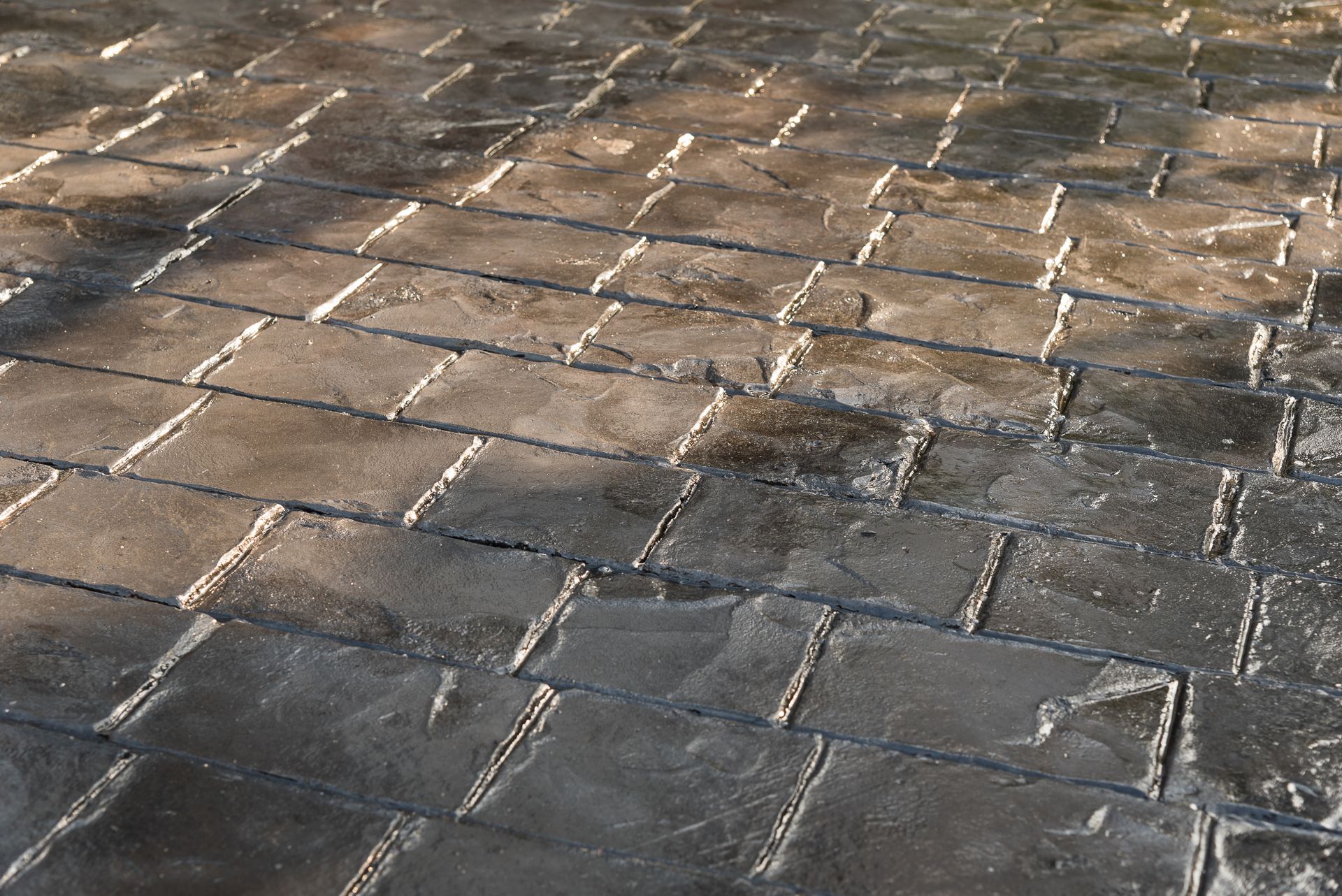 Wet stone pavement with sunlight reflections and a few dry patches