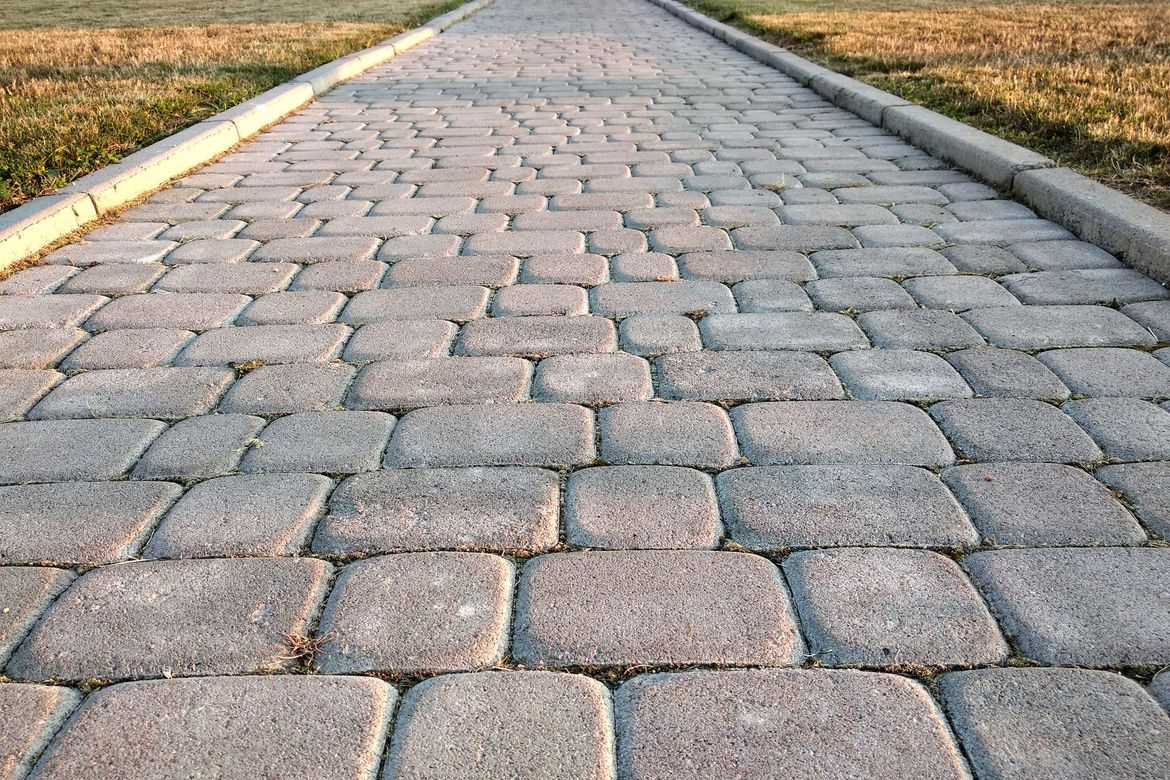 Stone-paved road stretching into the distance, bordered by yellow curbs and dry grass.