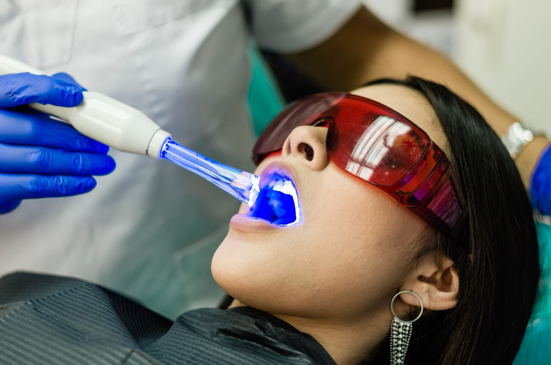 Woman undergoing teeth whitening with blue light in a dental office.