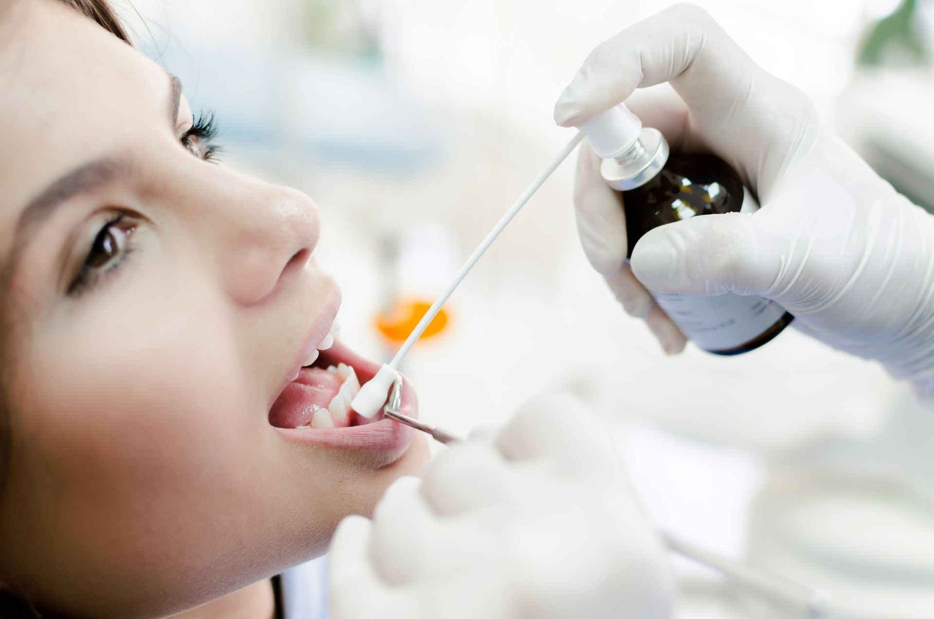 Dentist spraying a woman's open mouth with liquid. Hands in gloves, dental instruments, clinic setting.