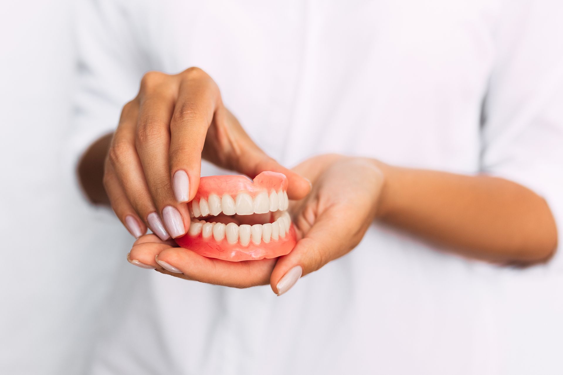 Hands holding a set of dentures, with pink gum-colored base and white teeth.