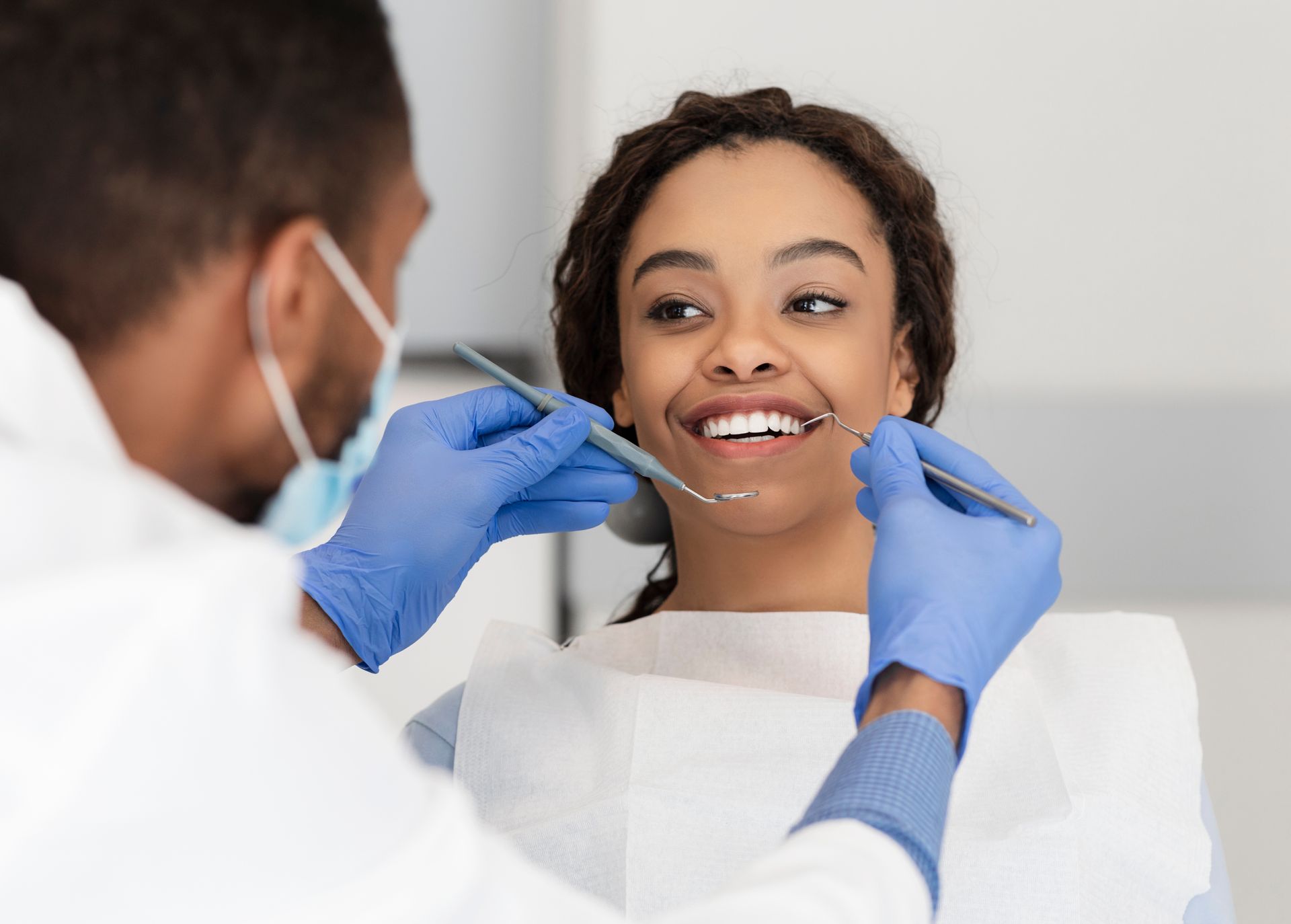 Dentist examining a patient's teeth. The patient smiles while the dentist holds tools.