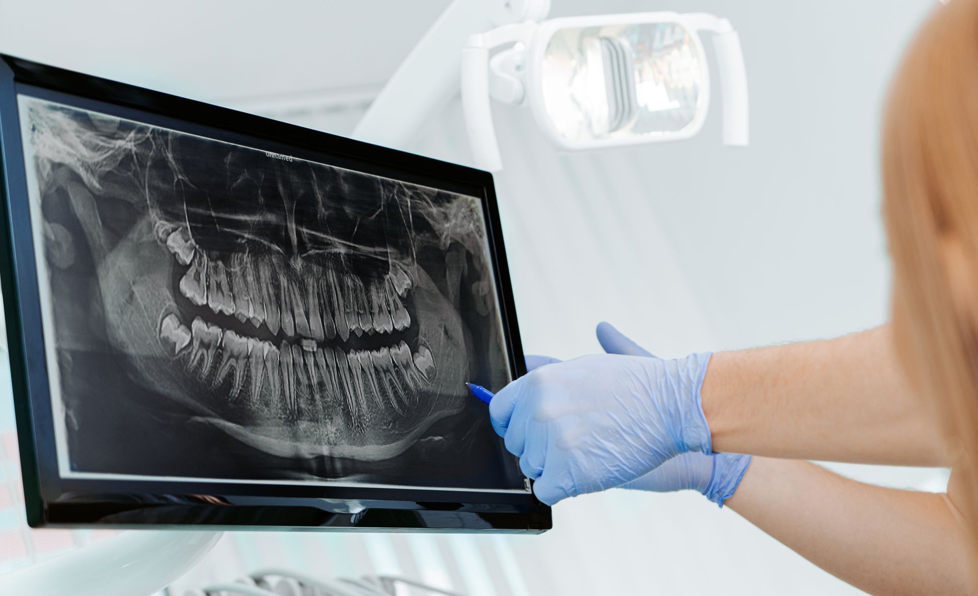 Dentist pointing to teeth on an X-ray screen; a patient looks on.