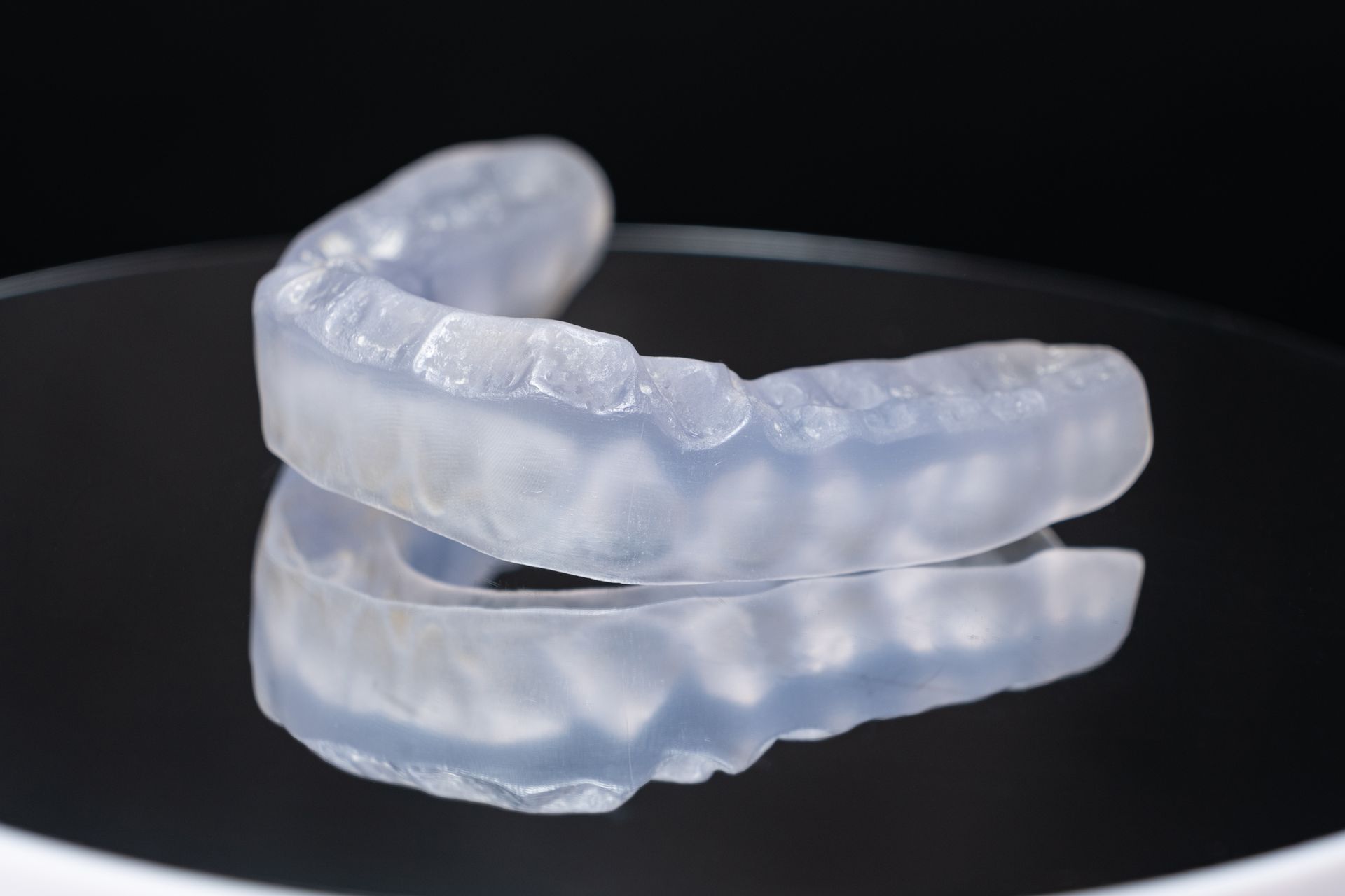 Clear plastic dental mouthguard, resting on a reflective surface.