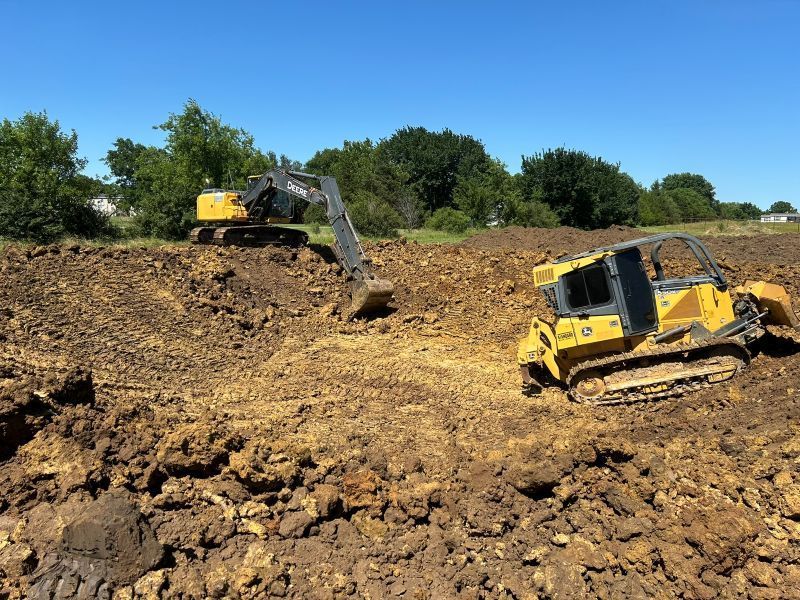 Two yellow bulldozers on a muddy construction site under a clear blue sky